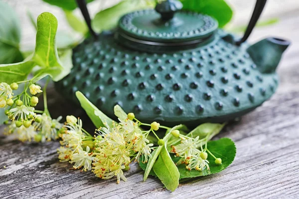 Teekanne mit Lindentee und Blumen auf altem Holzgrund — Stockfoto