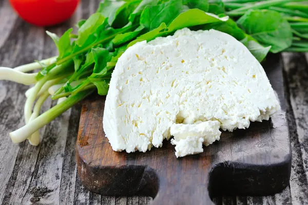 Cheese with arugula and onion on a wooden board — Stock Photo, Image