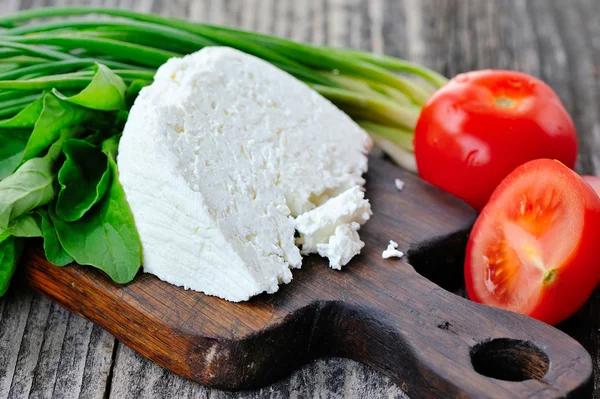 Cheese with tomatoes and arugula and onion on a wooden board — Stock Photo, Image