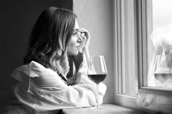漂亮的年轻姑娘带着一杯葡萄酒坐在窗边 黑白照片 — 图库照片
