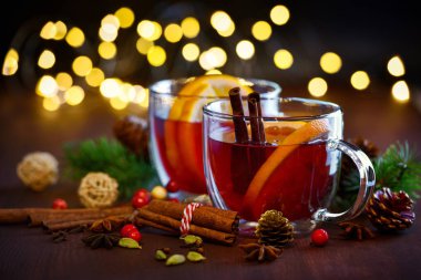 İçinde portakallı sıcak şarap ve ahşap arka planda baharatlar olan iki bardak Noel süslemeleri ile şenlik ışıklarının arka planında. Geleneksel sıcak içecek Noel zamanı