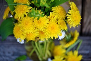 Bouquet of dandelion flowers, yellow wildflowers on old wooden table. Selective focus