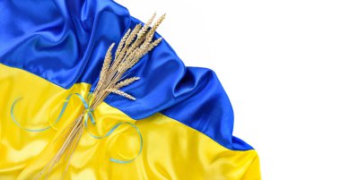 Bundle of wheat spikes with yellow and blue ribbon on the background of the flag of Ukraine isolated on white. Harvest of wheat and concept of Ukraine. Flat lay, copy space