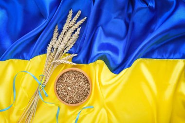 Wheat spikelets and bowl with wheat grains on the background of the flag of Ukraine. Harvest of wheat and concept of Ukraine