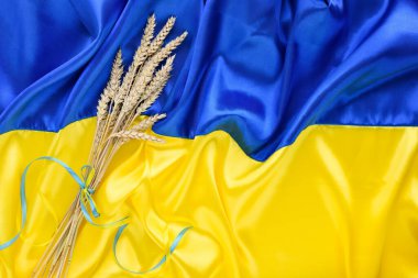 Bundle of wheat spikes with yellow and blue ribbon on the background of the flag of Ukraine. Harvest of wheat and concept of Ukraine. Flat lay, copy space