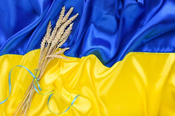 Bundle of wheat spikes with yellow and blue ribbon on the background of the flag of Ukraine. Harvest of wheat and concept of Ukraine. Flat lay, copy space