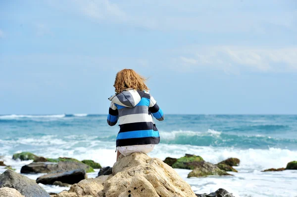 Mooie jonge vrouw zittend op de steen aan de kust — Stockfoto