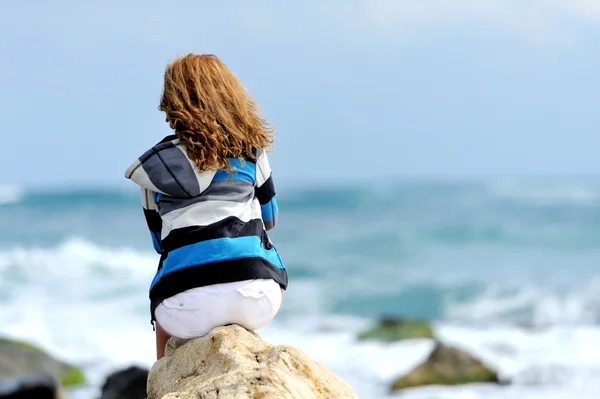 Young woman sitting on the stone on the seashore — Stock Photo, Image