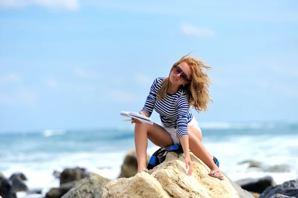 Mujer joven sentada en la piedra en la orilla del mar — Foto de Stock