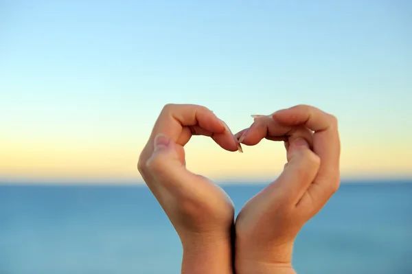 Mano femminile facendo una forma di cuore contro — Foto Stock