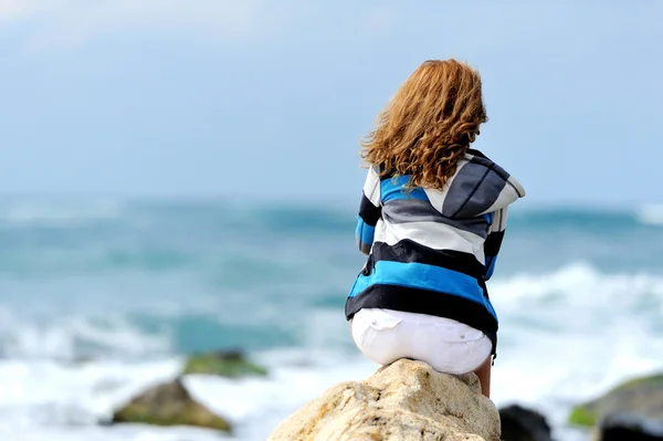 Mujer joven sentada en la piedra en la orilla del mar — Foto de Stock