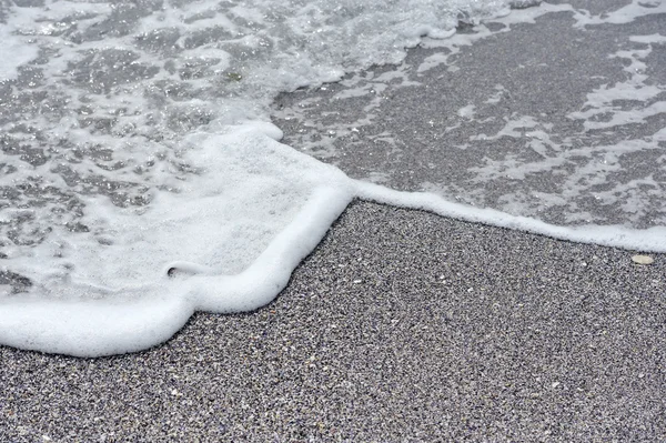 Schiuma di mare e ciottoli in una spiaggia — Foto Stock