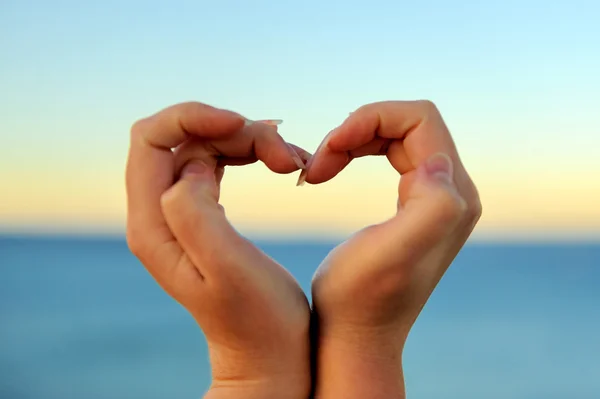 Mano femminile facendo una forma di cuore contro — Foto Stock