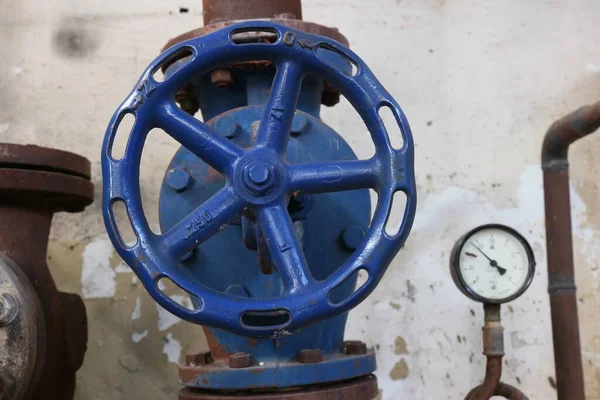 Borulara monte edilmiş mavi bir vana gri bir duvar arka planına karşı.