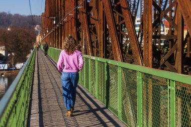 Genç bir kadın yaya köprüsünden tren yolunun yanına doğru yürüyor.