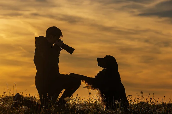 silhouette of a boy and a dog during sunset, photographer and takes a picture of the dog's head