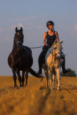 İki siyah beyaz atlı kadın boş bir arazide dörtnala koşuyor.