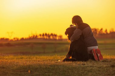 Gün batımında bir çocukla bir köpeğin silueti.