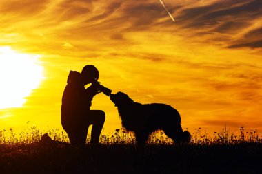 Gün batımında bir çocuk ve bir köpeğin silueti, fotoğrafçı kafasının yakın çekimini alır.