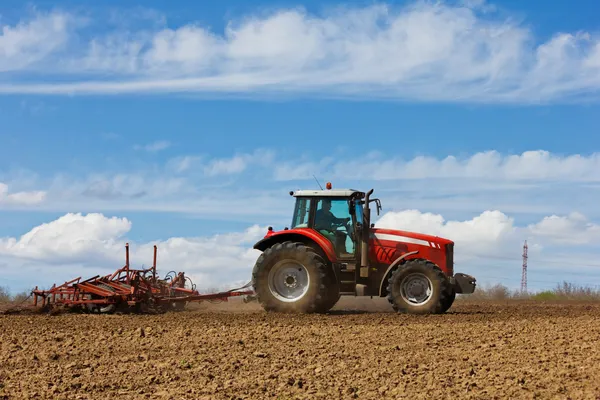 畑を耕す農家。畑でトラクターを栽培。農場の畑に耕された赤い農場トラクター。トラクターとプロー — ストック写真