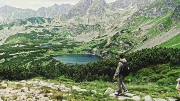 Aktive junge Touristen, ein Mann und eine Frau, steigen von einem malerischen Berg in Slomo den Hang hinunter, um sich im Sommer einen Bergsee näher anzusehen, Polen. — Stockvideo