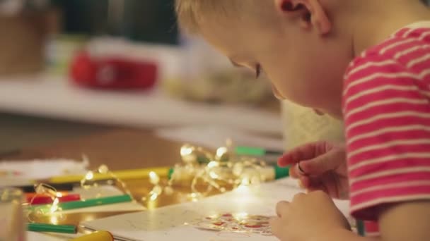 V předvečer nového roku doma, matka kreslí vánoční kresby s roztomilým synem předškolního věku, který lepí samolepky v podobě Santa Claus. — Stock video