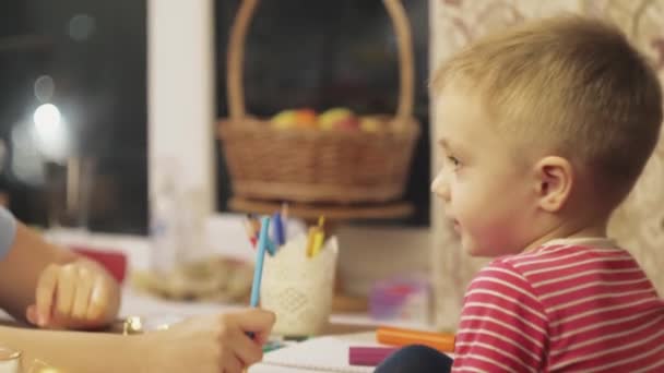 Zu Hause in der Küche an Silvester hilft eine Mutter ihrem süßen Sohn im Vorschulalter, schöne Weihnachtszeichnungen mit Bleistift zu zeichnen. — Stockvideo