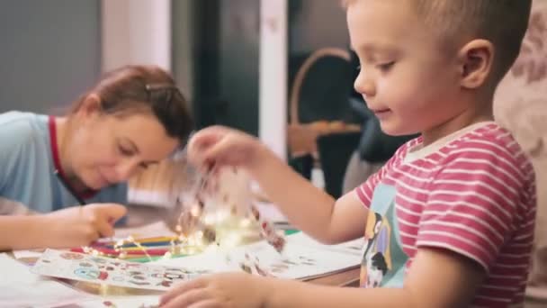 Após as férias de Ano Novo, mãe e filho se divertem, juntos desenhando e colando adesivos de vinil na forma de Papai Noel.. — Vídeo de Stock
