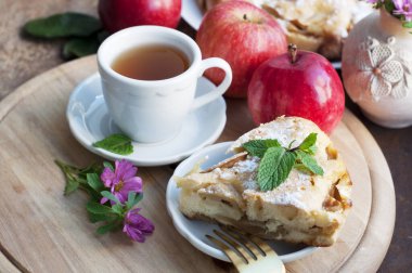 Elmalı turta, bir fincan çay, kırmızı elmalar ve kahverengi arka planda ahşap yuvarlak tahta çiçekler. Kırsal biçim