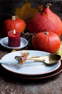 Balkabakları, kırmızı mum, sarı yapraklar, beyaz tabak ve altın bıçak, altın çatal, kahverengi arka planda altın kaşık.