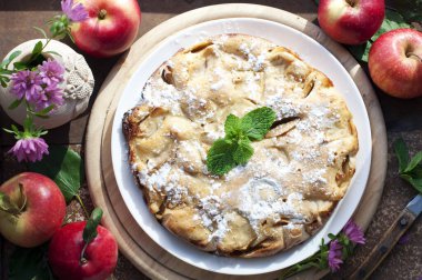 Elmalı turta, bir fincan çay, kırmızı elmalar ve kahverengi arka planda ahşap yuvarlak tahta çiçekler. Kırsal tarzda. Üst görünüm