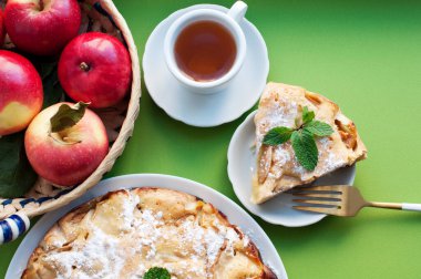 Elmalı turta, bir fincan çay, kırmızı elma ve yeşil arka planda çiçekler. Kırsal tarzda. Üst görünüm