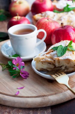 Elmalı turta, bir fincan çay, kırmızı elma ve ahşap arka planda çiçekler. Kırsal biçim
