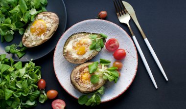 Beyaz bir tabakta yumurta, peynir, mısır salatası ve domatesle pişirilmiş avokado. Avokadoyla kahvaltı. Altın bıçak ve çatal. Üst görünüm