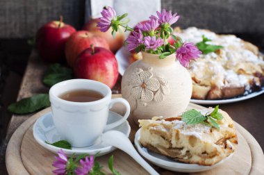 Elmalı ev yapımı kırmızı elmalı turta, bir fincan çay ve ahşap arka planda bir vazo çiçek. Kırsal biçim