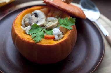 Fırınlanmış kabak dolması pirinç, havuç, biber ve mantar kahverengi tabakta maydanoz koyu kahverengi arka planda yuvarlak tahta üzerinde. Sağlıklı vejetaryen yemekleri. 