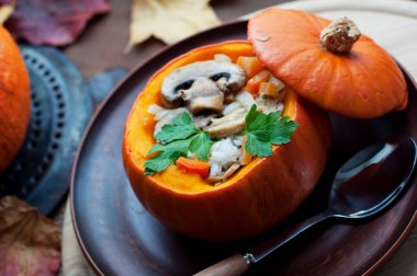 Fırınlanmış kabak dolması pirinç, havuç, biber ve mantar kahverengi tabakta maydanoz koyu kahverengi arka planda yuvarlak tahta üzerinde. Sağlıklı vejetaryen yemekleri. 
