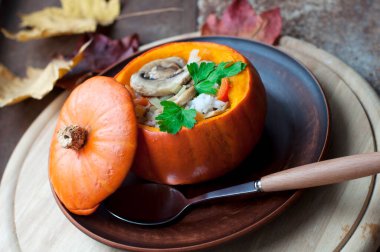 Fırınlanmış kabak dolması pirinç, havuç, biber ve mantar kahverengi tabakta maydanoz koyu kahverengi arka planda yuvarlak tahta üzerinde. Sağlıklı vejetaryen yemekleri. 