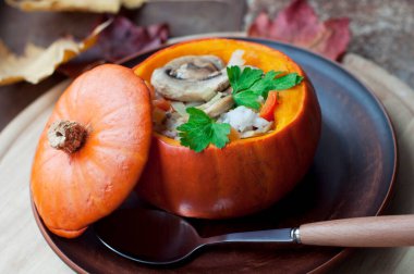 Fırınlanmış kabak dolması pirinç, havuç, biber ve mantar kahverengi tabakta maydanoz koyu kahverengi arka planda yuvarlak tahta üzerinde. Sağlıklı vejetaryen yemekleri. 