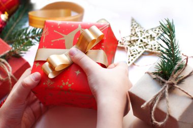 Çocukların elleri hediyelerle dolu bir kutuyu paketliyor. Kırmızı, altın ve bej renkli kutular kurdeleli, boncuklu, yıldızlı, köknar dallı. Beyaz bir arka planda yılbaşı süsleri olan Noel hediyeleri. Üst görünüm