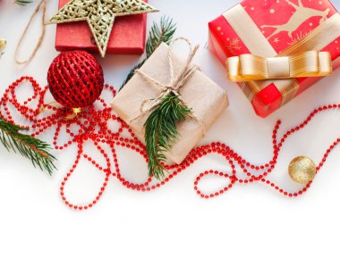 Kırmızı, altın ve bej renkli kutular kurdeleli, boncuklu, yıldızlı, ladin dallı. Beyaz bir arka planda yılbaşı süsleri olan Noel hediyeleri. Mesaj için yer. Üst görünüm