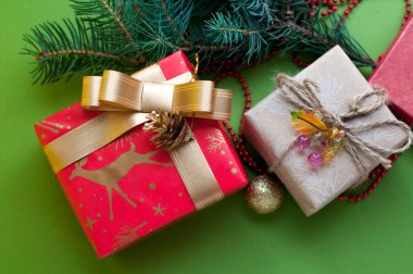 Kırmızı ve bej renkli kutular, kurdeleler, boncuklar, ladin dalları. Yeşil arka planda yılbaşı süsleri olan Noel hediyeleri. Mesaj için yer. Üst görünüm