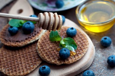 Çikolatalı waffle, bal, nane, kızılcık, ahududu ve yaban mersini, koyu kahverengi arka planda. Waffle 'lı romantik kahvaltı ve tahta tahtada meyveler. Tatlının üzerine bal damlıyor.