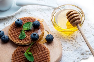 Çikolatalı waffle, yaban mersini, beyaz dantelli bal. Bir fincan çayla romantik kahvaltı, bal çubuğu, waffle üzerine meyveler.