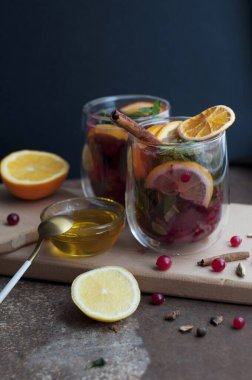 Koyu kahverengi arka planda kızılcık, portakal, limon, tarçın, bal ve naneli çay. İki bardak meyve çayı ve ahşap tahtada baharat.