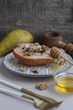 Mavi peynirli armut, bal ve gri arka planda ceviz. Çatallı, bıçaklı armut.