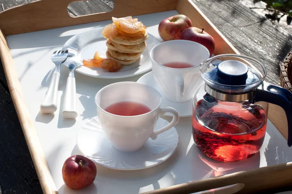 Country breakfast with pancakes, apple jam and tea on a wooden table. Rustic breakfast outdoors on tray