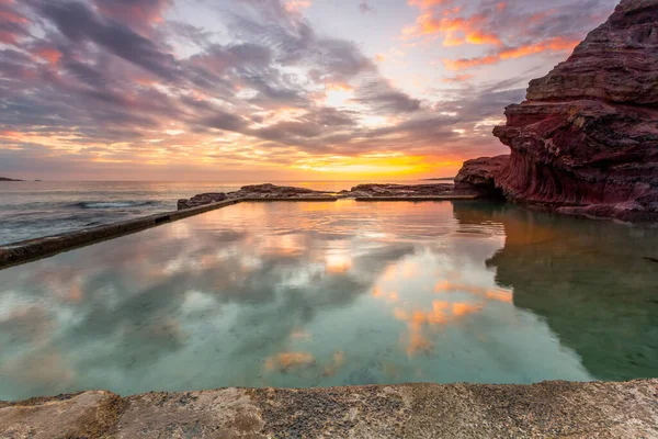 Ocean rock pool built into cliffs with small cave and sunrise reflections — Stock Photo, Image