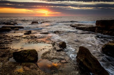 Güneş, bulutların arasından kayalık sahillere doğru bir göz atıyor.