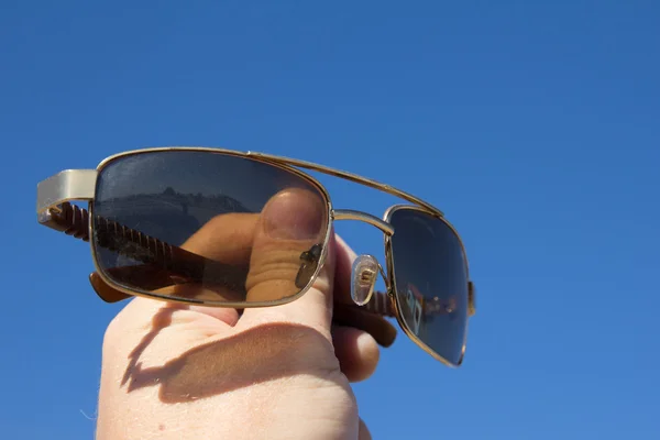 Okulary w ręku człowieka na tle niebieskiego nieba — Zdjęcie stockowe